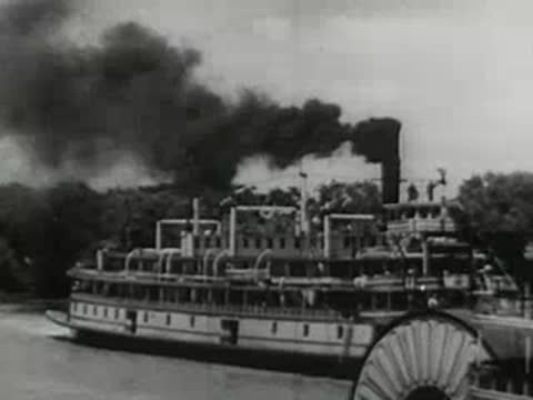 close-up of a large paddle steamer moving along a river with smoke from its chimney