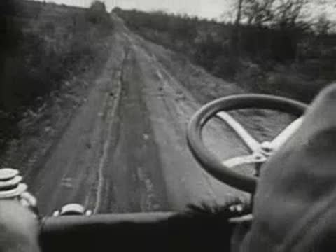 Driver's POV behind the steering wheel of an early vintage automobile on a dirt road