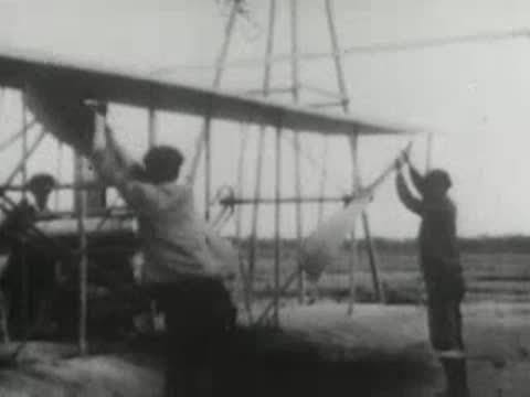 Men starting and preparing a pioneering biplane for flight on an open field