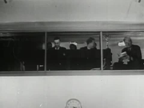 Men in control room watching and reading documents through large windows, broadcasting station