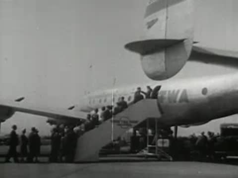 Passengers boarding a vintage TWA propeller airplane via mobile stairs, 1940s style.