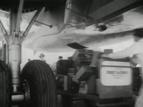 Airport workers loading luggage into the belly compartment of a propeller airplane, 1940s.