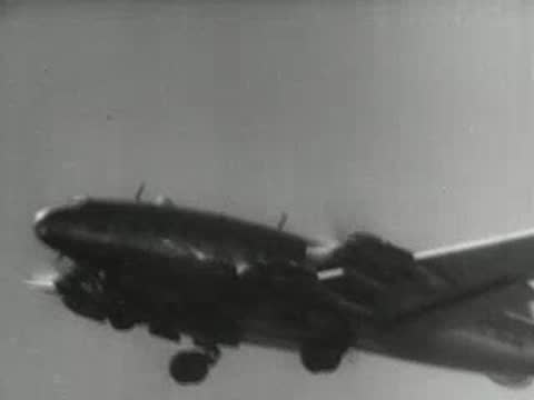 Four-engine propeller airplane in flight against a bright sky, 1940s aviation documentary.