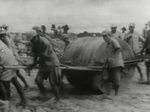 Workers pulling a heavy cylindrical roller with ropes
