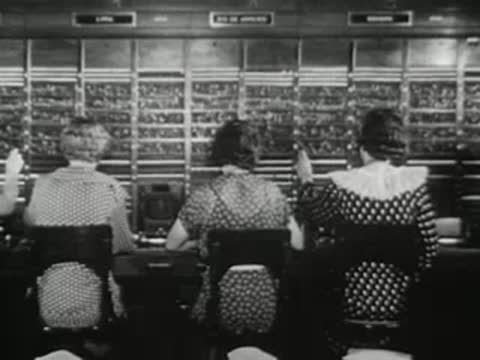 Telephone operators working at a large switchboard console, mid-20th century office.
