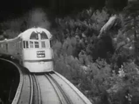 Streamlined passenger train traveling on a curved track through a forest, 1940s.