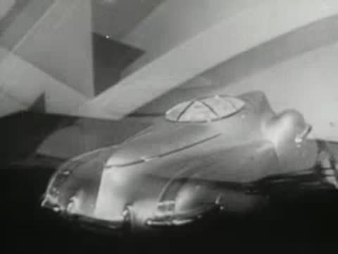futuristic streamlined car model rotating on turntable against abstract geometric backdrop