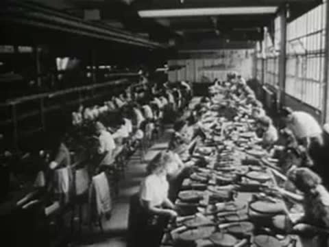large factory interior with rows of workers assembling items at long tables