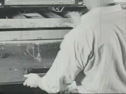 A worker sliding wooden trays of eggs into an industrial incubator machine