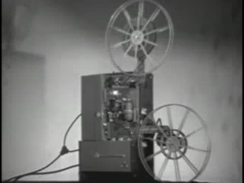 Projector rolling film with reels spinning in a room.