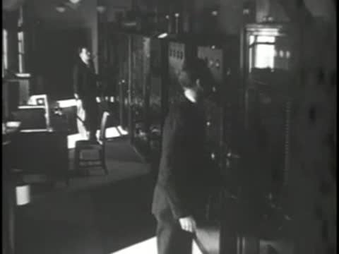 A man in a suit walks into a television control room.