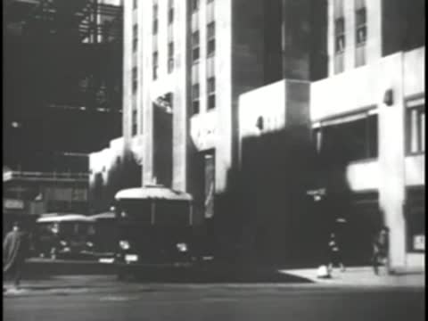 Street level view of a large stone building with buses passing by.