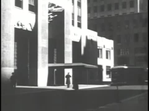 A city street corner with a pedestrian standing near modernistic buildings.