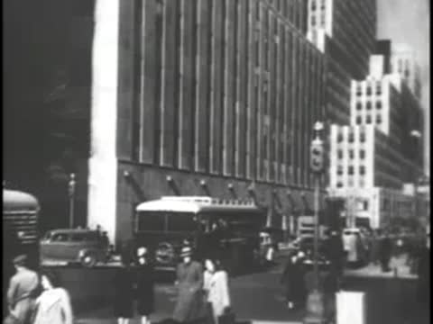 Busy city street scene with pedestrians walking and traffic passing by.