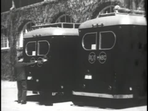 Crew members stand near the rear doors of parked RCA television vans.