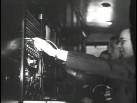 A technician operates a patch bay or switchboard with cords.