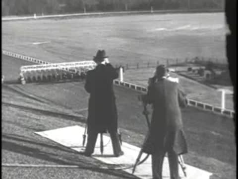 Men looking through binoculars and camera towards racetrack in the distance