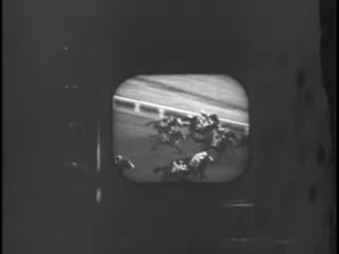 Television monitor displaying live footage of racehorses running on a racetrack