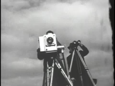 Cameraman filming outdoors with vintage broadcasting camera and binoculars nearby