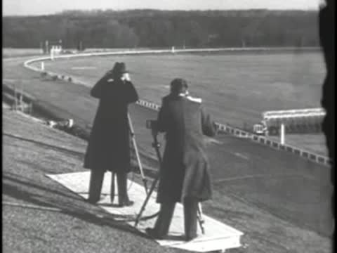 Men standing on platform with binoculars and camera overlooking a racecourse