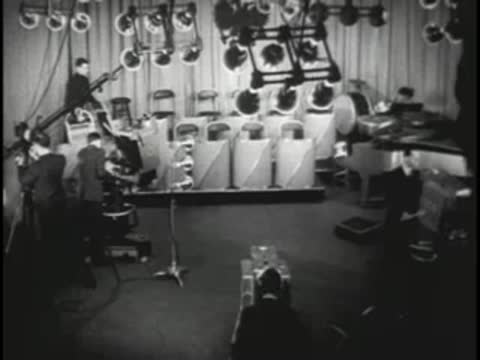 Studio stage with musical instruments, lighting rigs, and crew members working