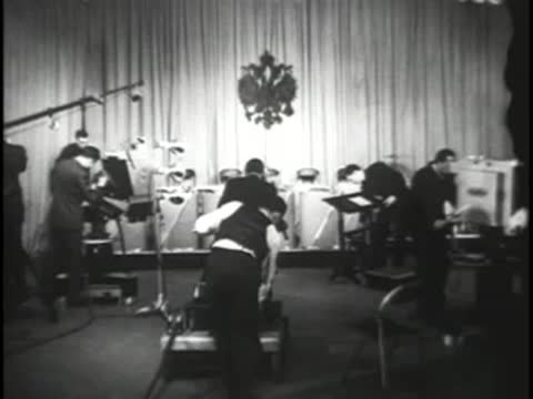 Studio crew working around musical instruments and equipment in front of curtain