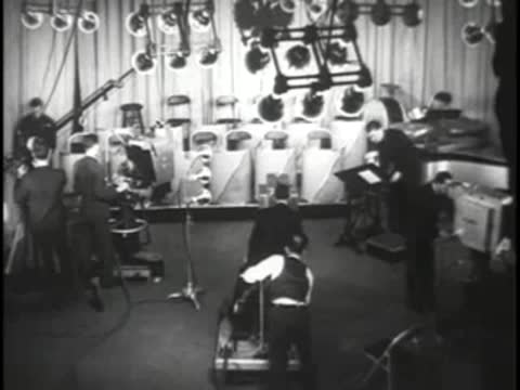 Studio production scene with camera equipment, crew, and stage lighting overhead