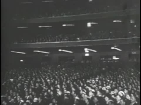 Large audience seated in a darkened theater or auditorium.