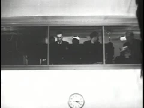 Control room staff looking through glass window with a wall clock visible
