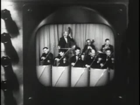 Television studio camera shooting a live orchestra performance with musicians.