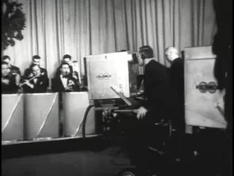 Cameramen operating large television cameras during a live orchestra studio broadcast.