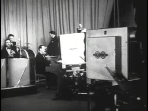 Studio camera operator filming an orchestra performance on a set.