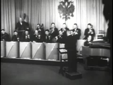 Full orchestra playing on a television studio stage with a conductor.