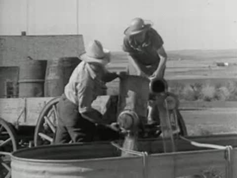 People pouring water from containers into a tank on a farm, 1930s era