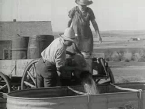 People pouring water into a trough near a windmill, historical footage