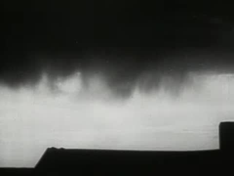 Wide shot of dark, heavy storm clouds rolling low over a rural landscape, 1930s