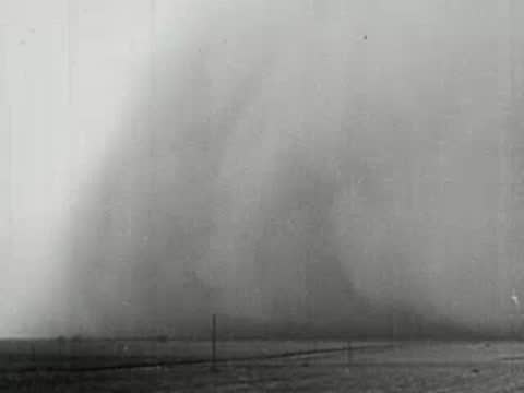 Wide shot of a massive dust storm wall advancing across a flat plain, 1930s