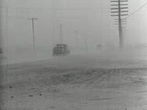 Wide shot of a car driving down a dusty road during a storm, 1930s