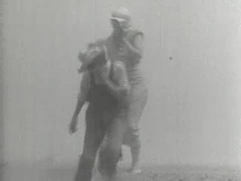 Medium shot of two people shielding their faces while walking through a dust storm, 1930s