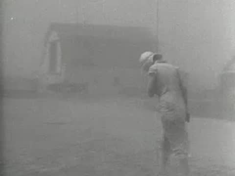 Medium shot of a person walking alone through a hazy, dust-filled landscape, 1930s
