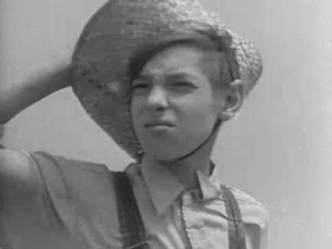 Close-up portrait of a young boy wearing a straw hat outdoors, 1930s