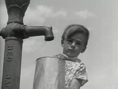 Close-up of a young child looking at the camera next to a water pump