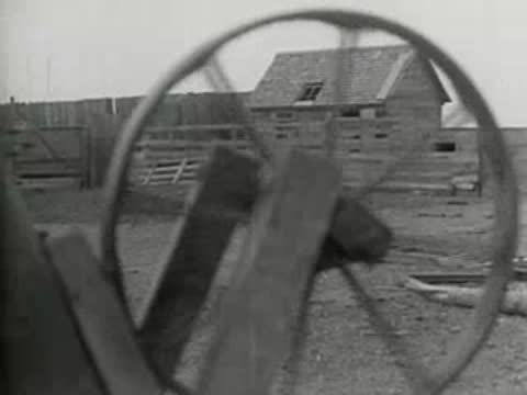 Close-up of a wooden wagon wheel turning with a farm building behind