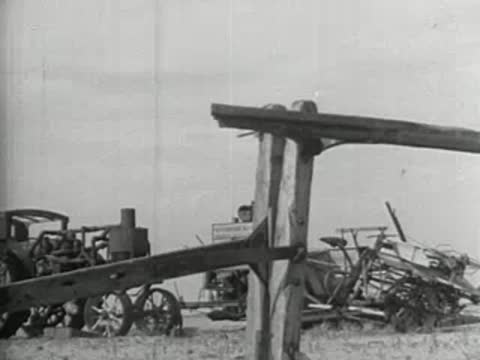 Vintage farm equipment viewed through a wooden structure, black and white footage.