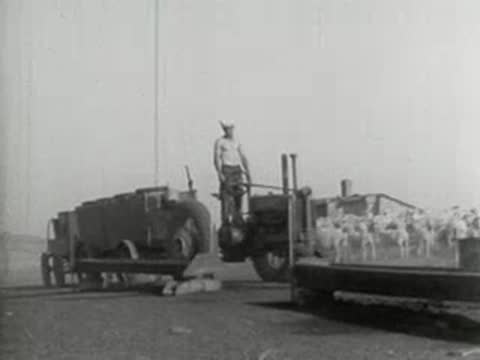 A man operating an old farm tractor with a large wagon attached.