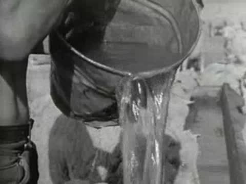A person pouring water from a bucket into a trough for livestock.
