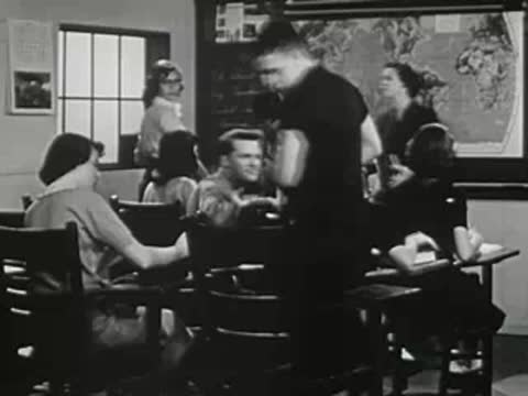 Students standing up and interacting at desks in classroom.