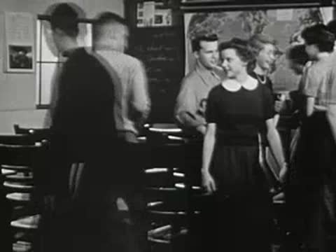 Students standing and walking around desks in classroom.