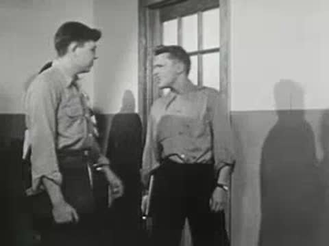 Two students standing and talking in hallway near door.