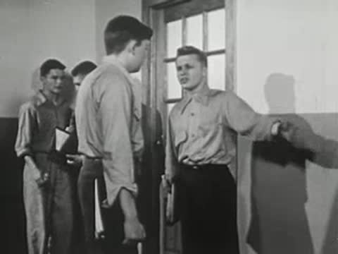 Two students standing in hallway conversing near doorway.